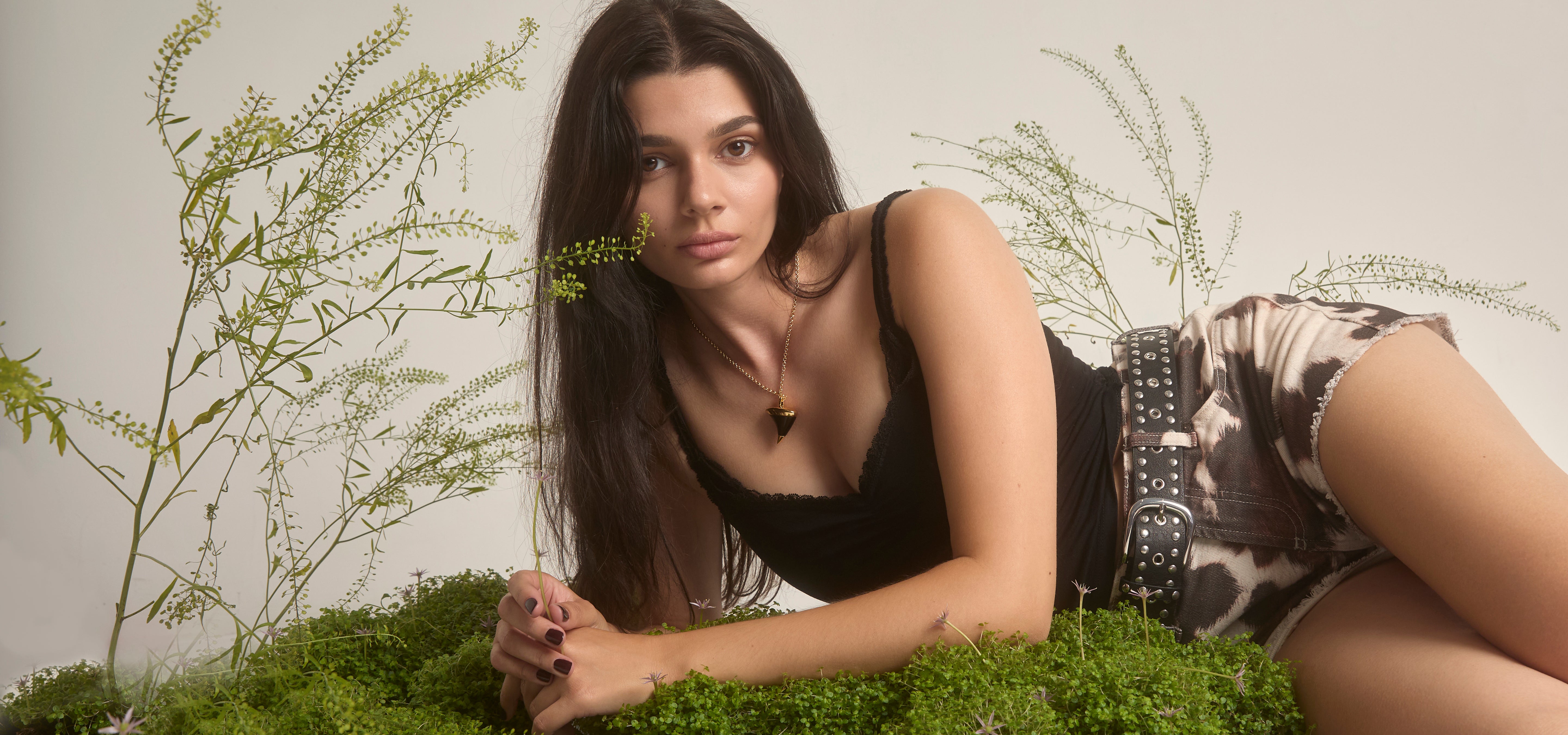 Woman lying on grass with plants around, wearing a black top and patterned shorts.
