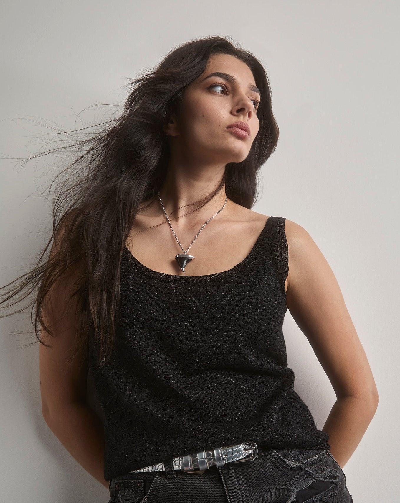 Woman wearing a black tank top and ripped black shorts against a plain background. wearing a large oxyn thorn necklace.