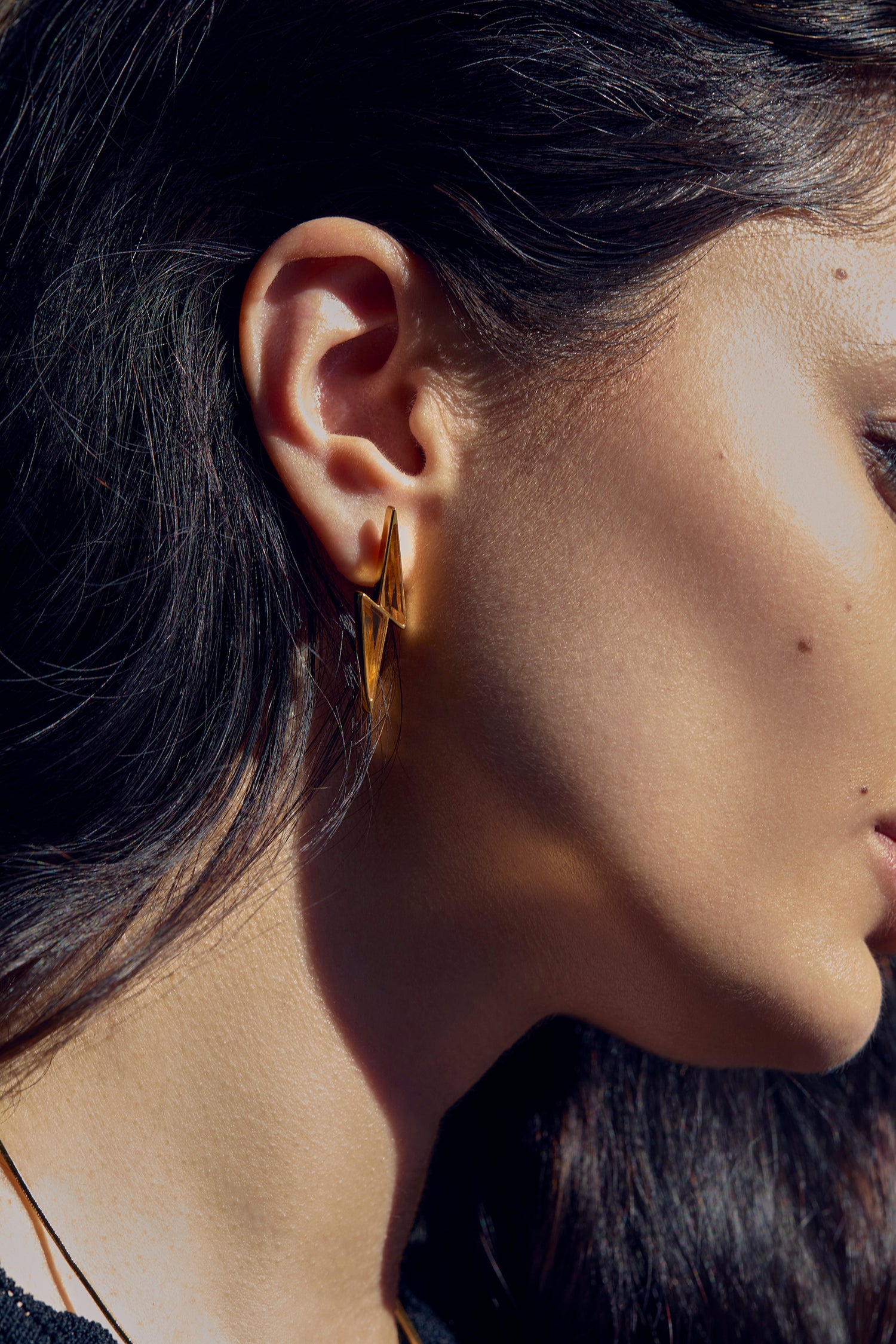 Close-up of a person wearing gold earrings with a neutral background