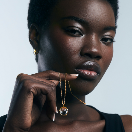 Woman wearing a gold necklace with a pendant against a neutral background