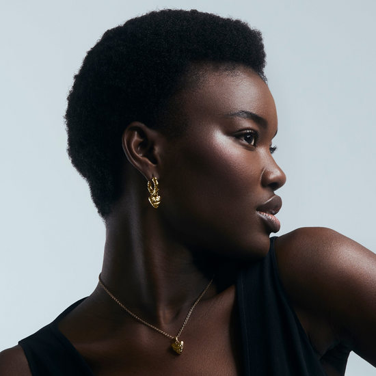 Woman wearing gold heart pendant with thorns wrapped around  against a neutral background