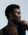 Woman wearing gold heart pendant with thorns wrapped around  against a neutral background