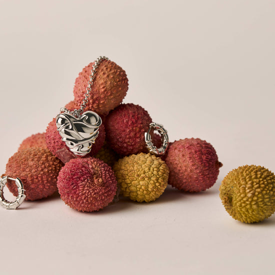 Silver jewelry pieces on lychee fruits against a neutral background