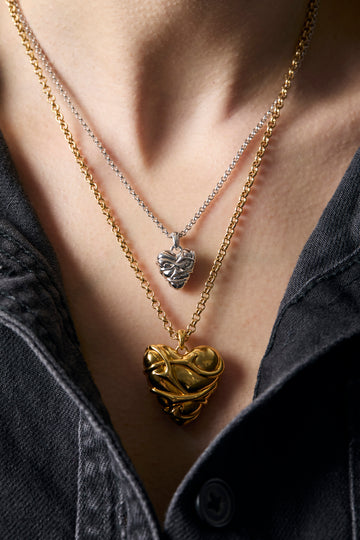 Gold heart pendant necklace on a person wearing a dark denim shirt.