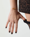Hand with black nail polish wearing a gold bracelet on a plain background