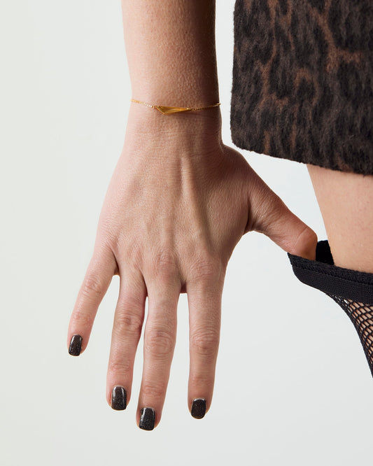 Hand with black nail polish wearing a gold bracelet on a plain background