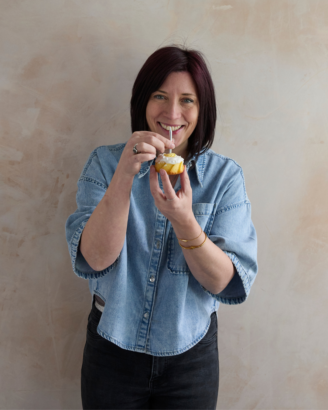Woman holding a small cupcake with a straw against a beige wall