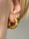 Close-up of a person wearing gold hoop earrings with a blurred background