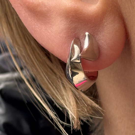 Close-up of a person wearing a silver earring with a pink interior.