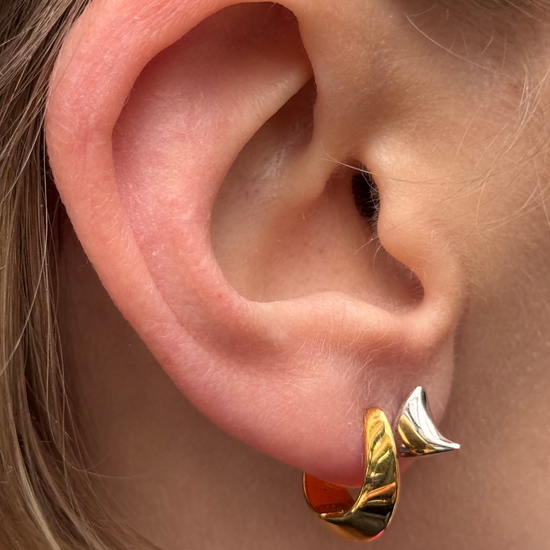 Close-up of an ear with gold hoop earrings and a hair accessory.