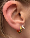 Close-up of an ear with gold hoop earrings and a hair accessory.