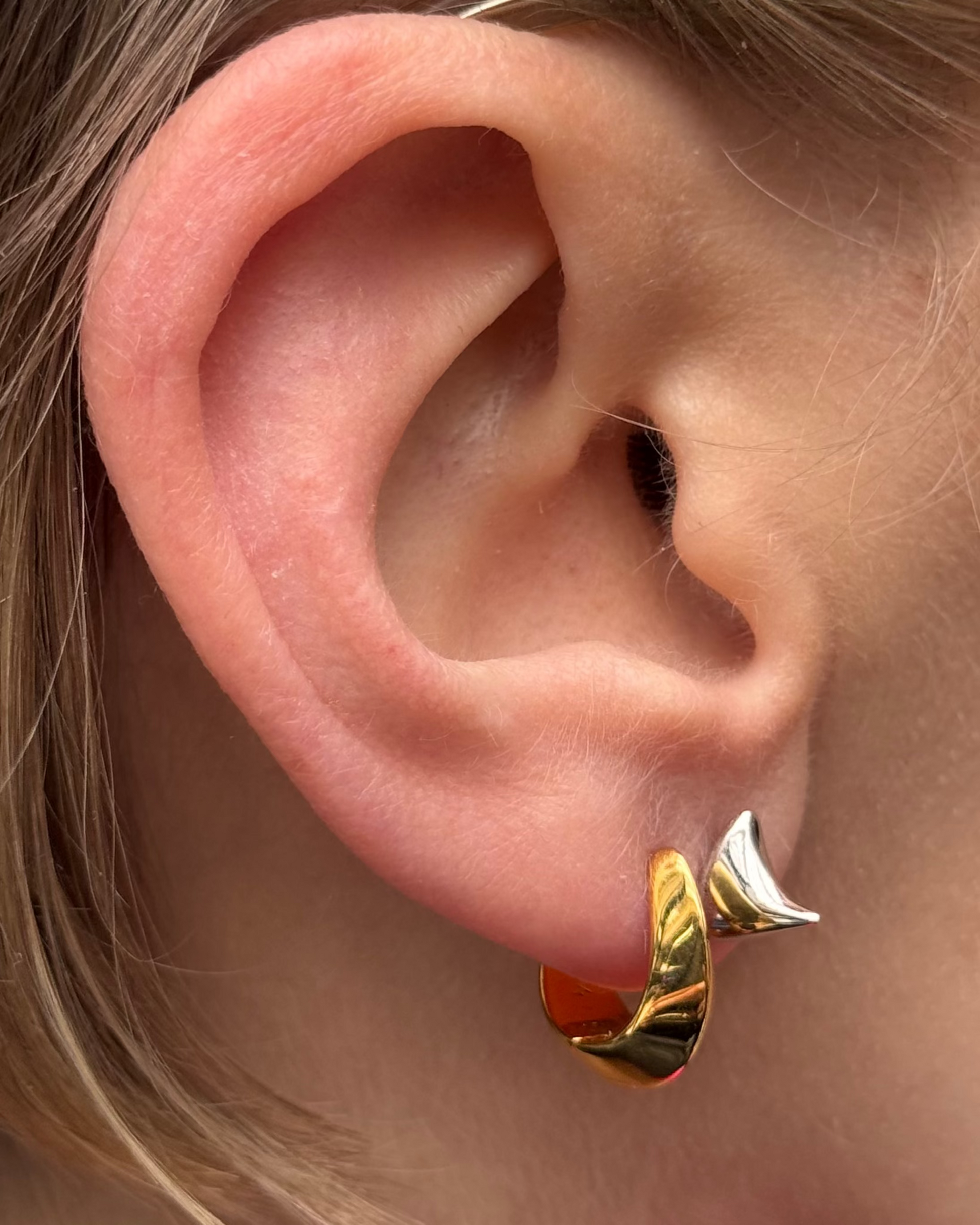 Close-up of an ear with gold hoop earrings and a hair accessory.