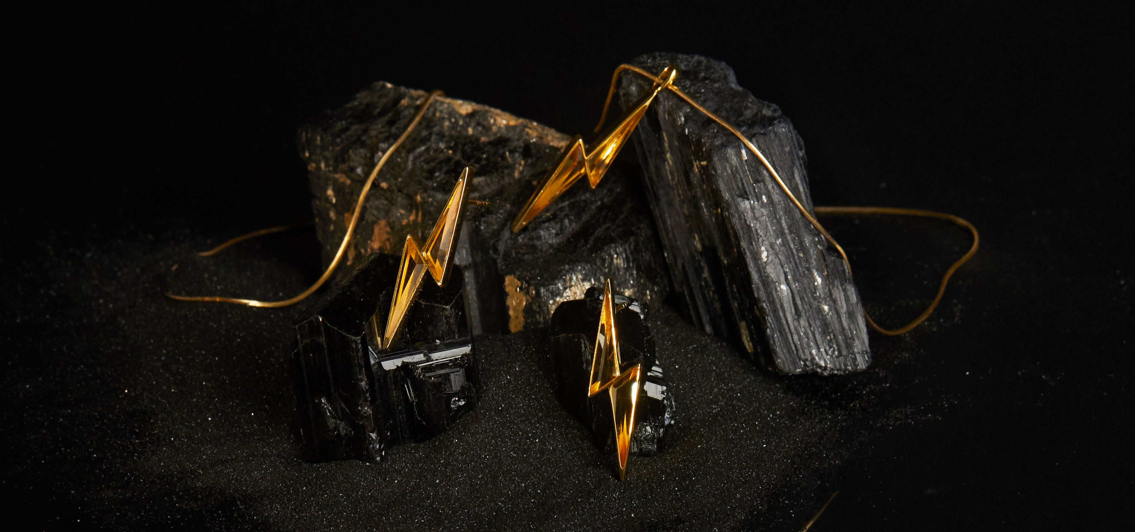Gold lightning bolt earrings and necklace on black stone with a dark background