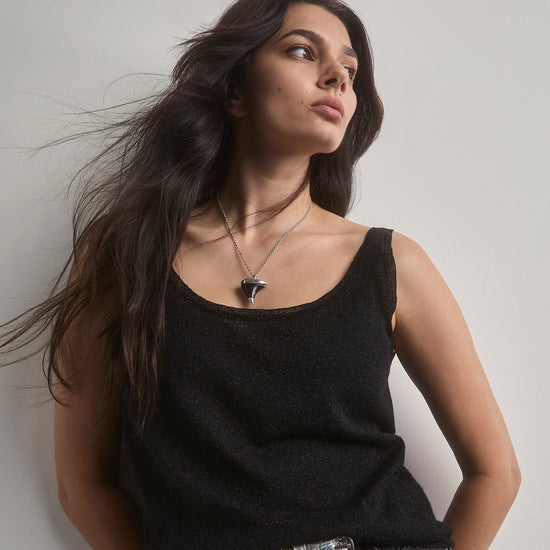 Woman wearing a black tank top and ripped black shorts against a plain background. wearing a large oxyn thorn necklace. 