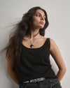 Woman wearing a black tank top and ripped black shorts against a plain background. wearing a large oxyn thorn necklace. 