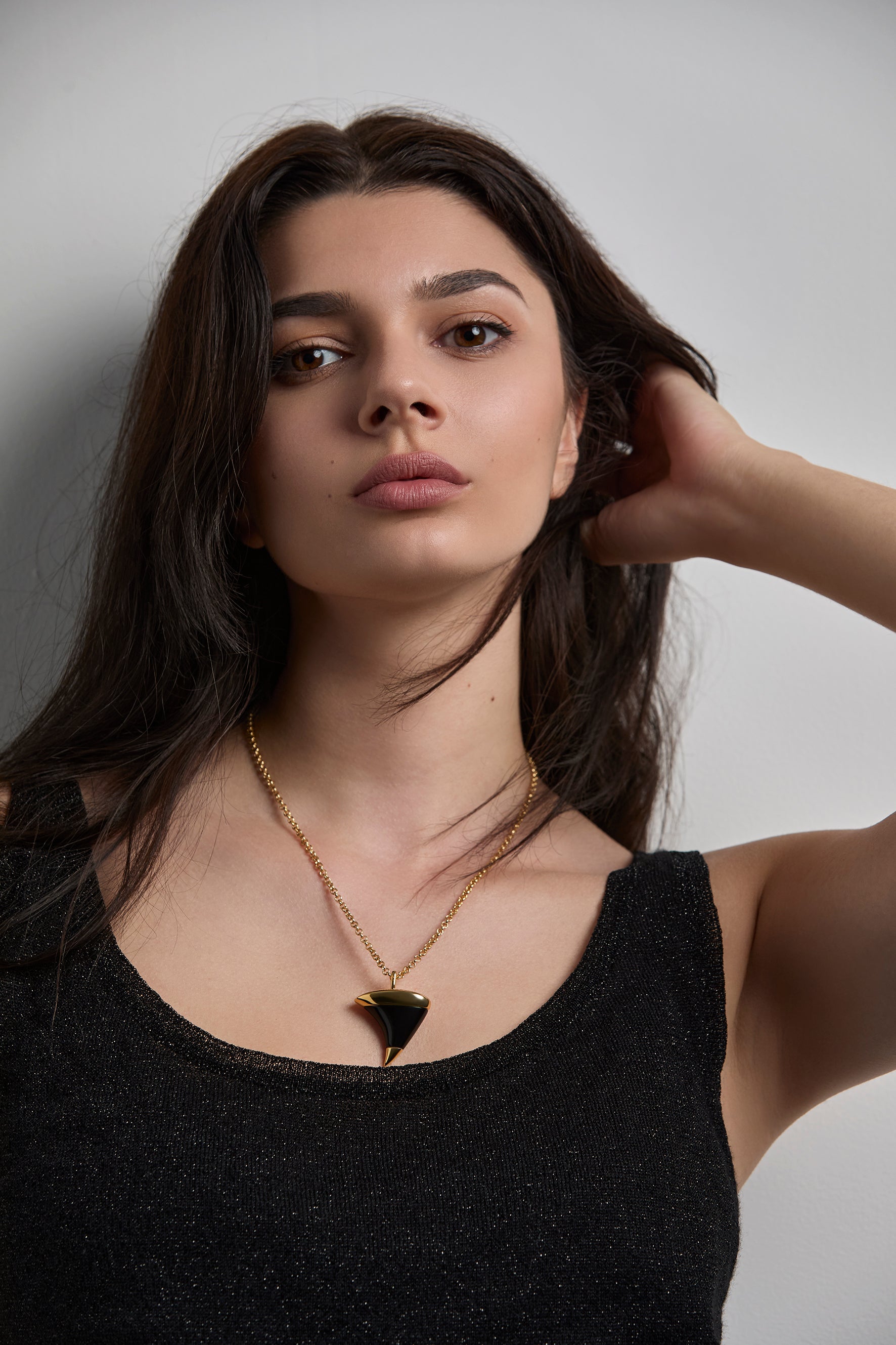 Woman wearing a  gold necklace with an onxy stone. shaped like a thorn against a neutral background