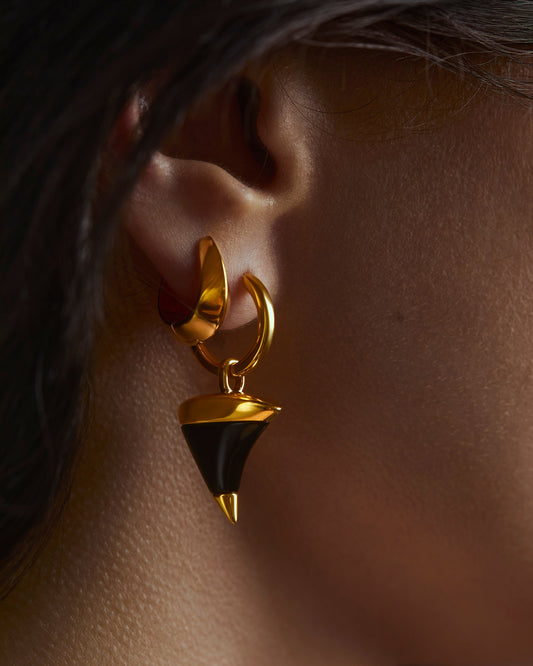 Gold and black earring worn on an ear with a blurred background