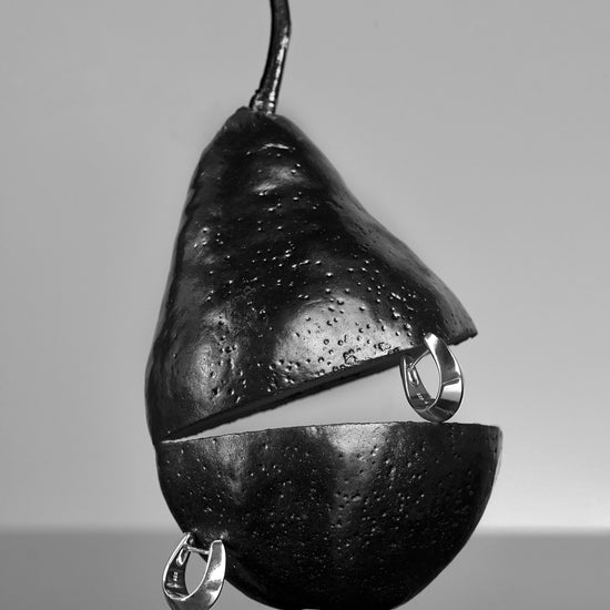 Metallic pear-shaped object with hanging rings on a reflective surface