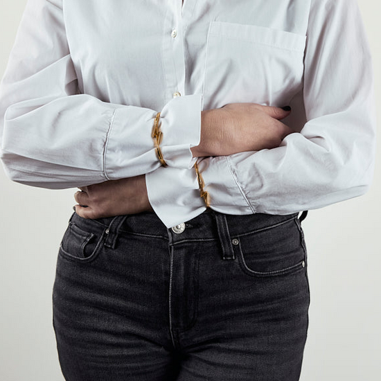 Person wearing a white button-up shirt with rolled-up sleeves and dark jeans against a plain background
