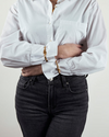 Person wearing a white button-up shirt with rolled-up sleeves and dark jeans against a plain background