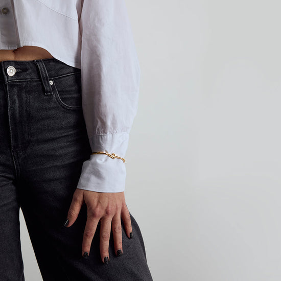 Person wearing a white shirt and black jeans against a plain background. Gold Vermeil bangle with a citrine lightning bolt.