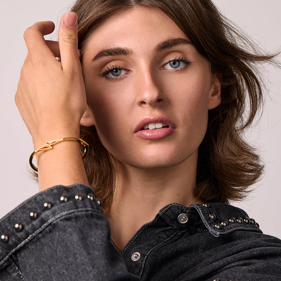 Woman wearing a black denim jacket with studded details, with a citrone thunderbolt bangle on a plain background