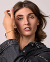 Woman wearing a black denim jacket with studded details, with a citrone thunderbolt bangle on a plain background