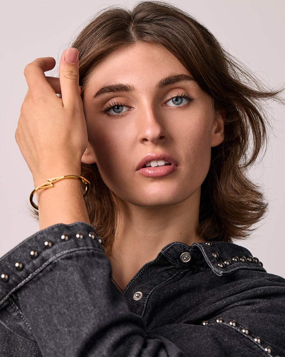 Woman wearing a black denim jacket with studded details, with a citrone thunderbolt bangle on a plain background