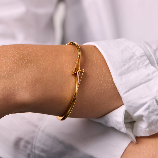 Gold bracelet with citrine thunderbolt shaped bangle on a wrist with a blurred white background