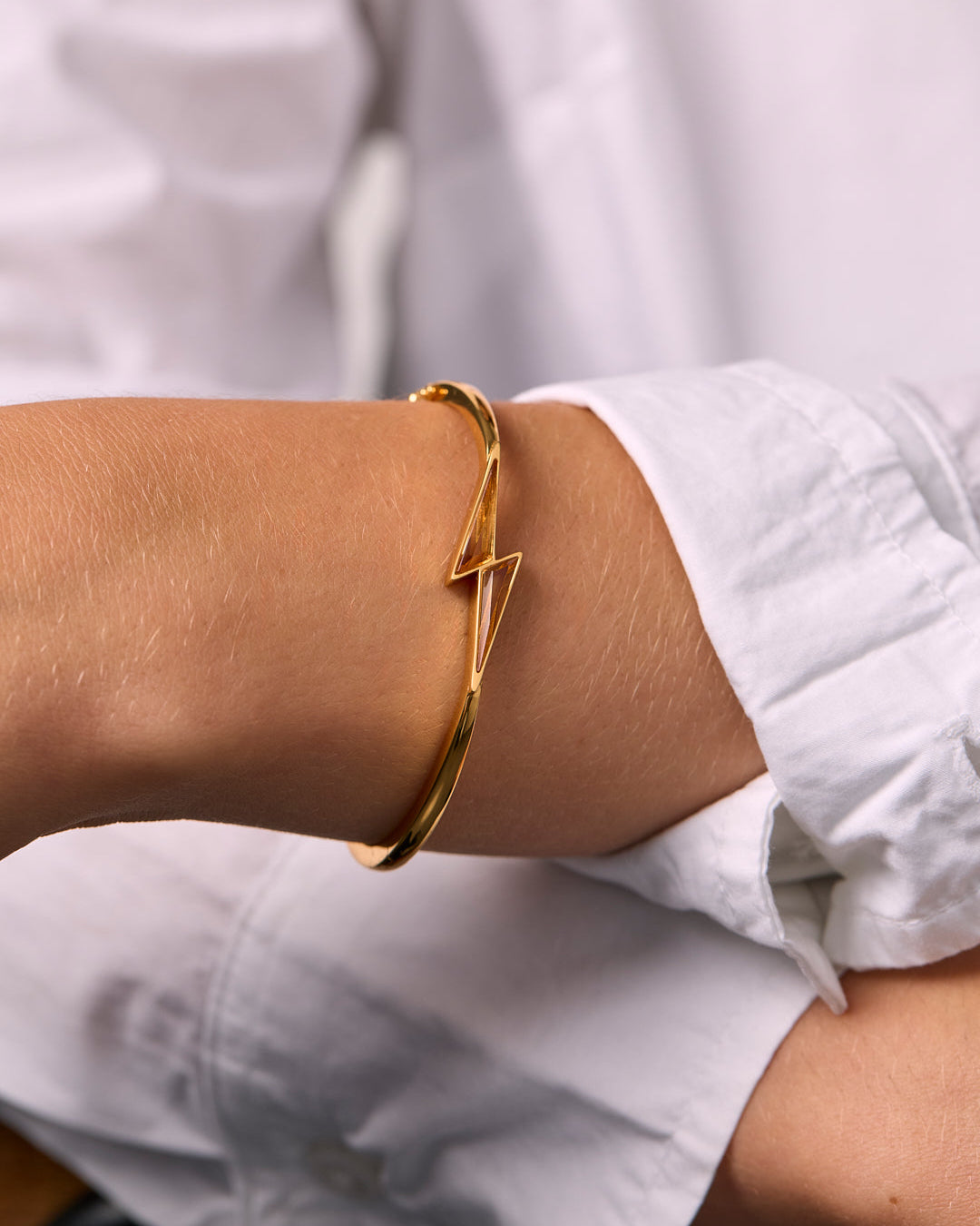 Gold bracelet with citrine thunderbolt shaped bangle on a wrist with a blurred white background