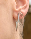 Close-up of an ear wearing a silver arrow-shaped earring with a blurred background