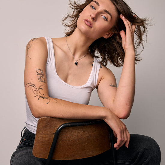 Woman sitting on a chair against a plain background wearing a black only, thorn  shape necklace