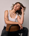 Woman sitting on a chair against a plain background wearing a black only, thorn  shape necklace