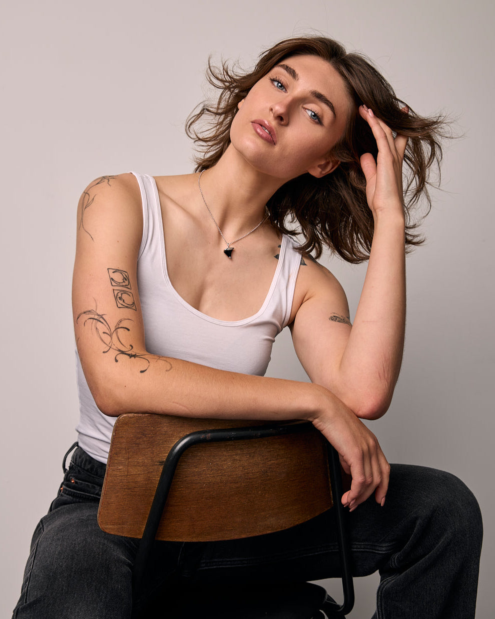 Woman sitting on a chair against a plain background wearing a black only, thorn  shape necklace