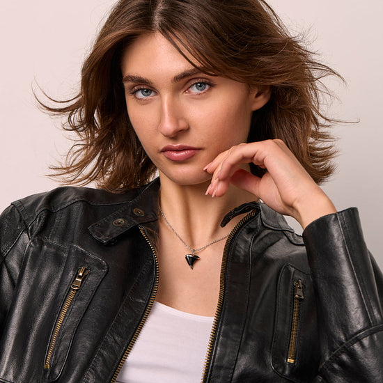 Woman wearing a black leather jacket and a black thorn shape onyx pendant/ against a neutral background
