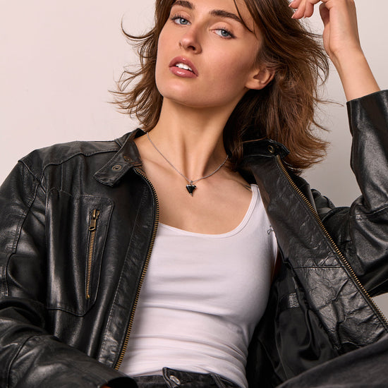 Woman wearing a black leather jacket over a white top, sitting against a plain background