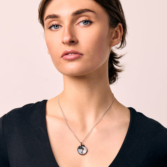 Woman wearing a black long-sleeve top and a necklace with a moon pendant on a beige background