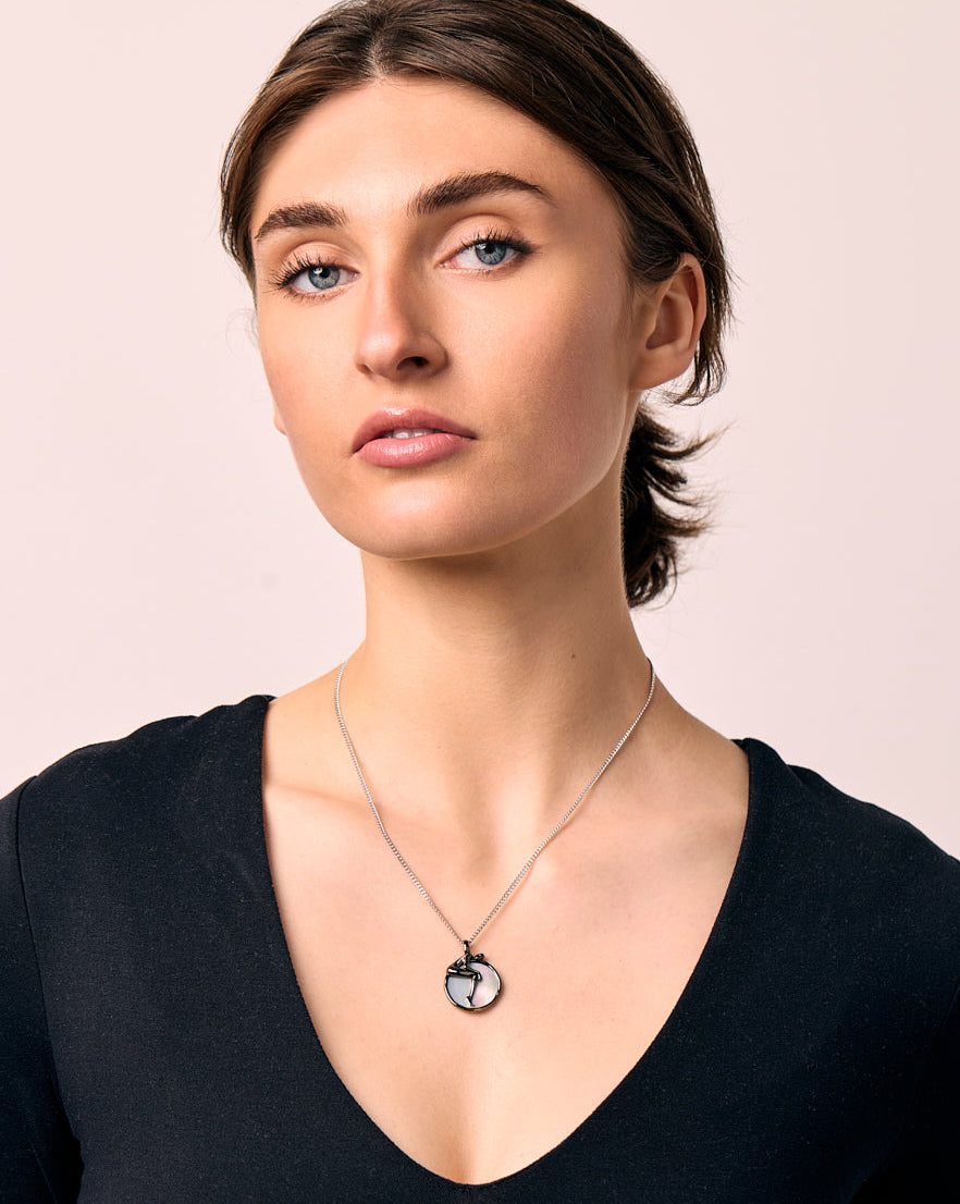 Woman wearing a black long-sleeve top and a necklace with a moon pendant on a beige background