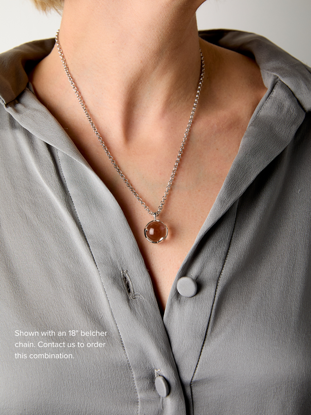 Necklace with a round pendant worn by a person in a gray shirt.