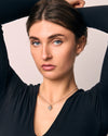 Woman wearing a black top and small heart pendant with her arms raised, against a plain background