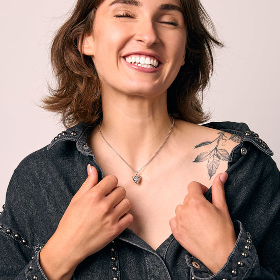 Woman wearing a dark denim jacket with a heart pendant on a plain background