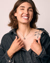 Woman wearing a dark denim jacket with a heart pendant on a plain background