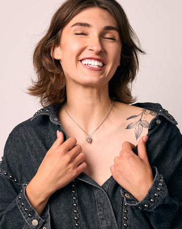 Woman wearing a dark denim jacket with a heart pendant on a plain background