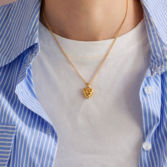 Person wearing a gold heart-shaped necklace with a blue and white striped shirt.
