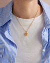 Person wearing a gold heart-shaped necklace with a blue and white striped shirt.