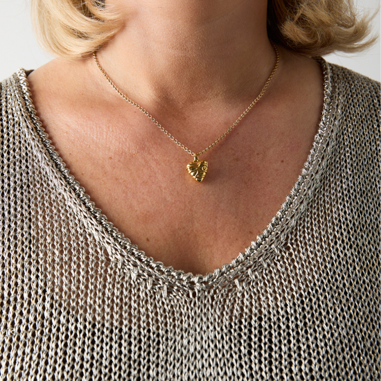 Close-up of a person wearing a gold necklace with a heart pendant.