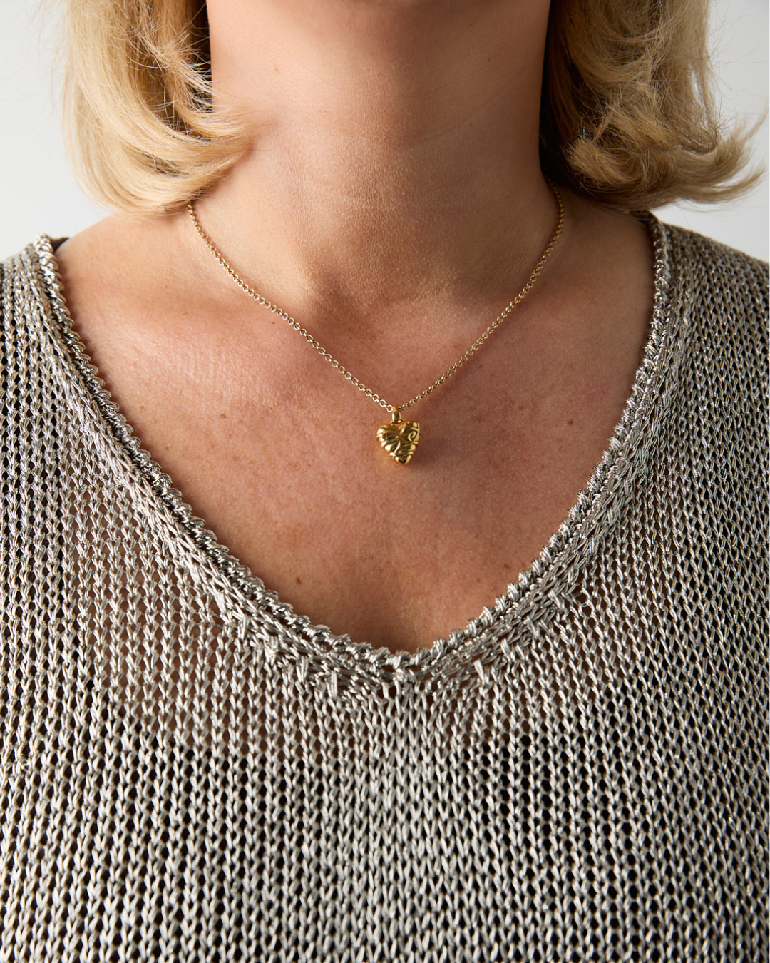 Close-up of a person wearing a gold necklace with a heart pendant.