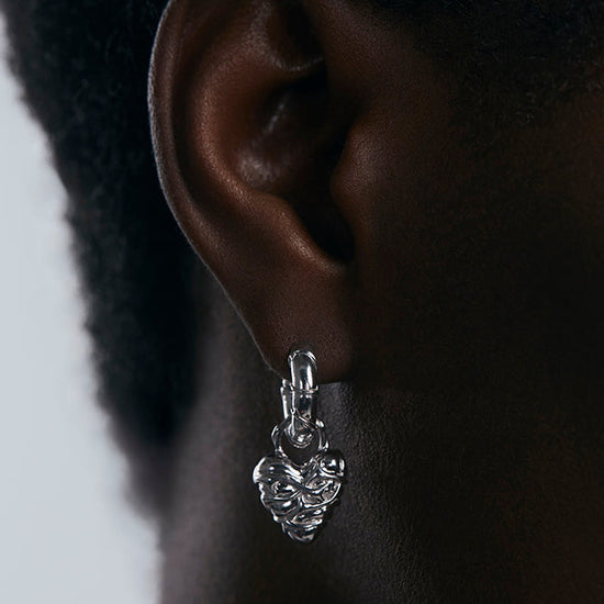 Silver earring worn on an ear with a neutral background