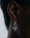 Silver earring worn on an ear with a neutral background
