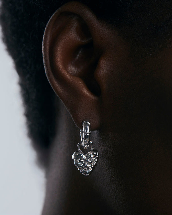 Silver earring worn on an ear with a neutral background